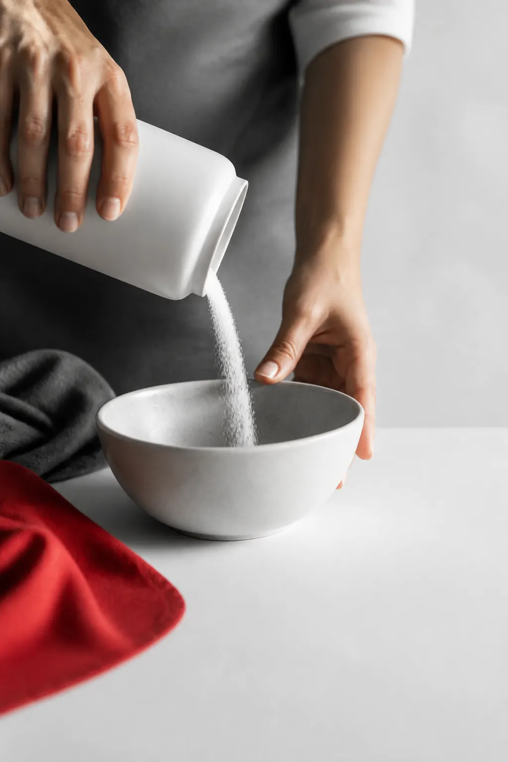 Manos vierten el contenido de un envase blanco sin marca en un recipiente sencillo.