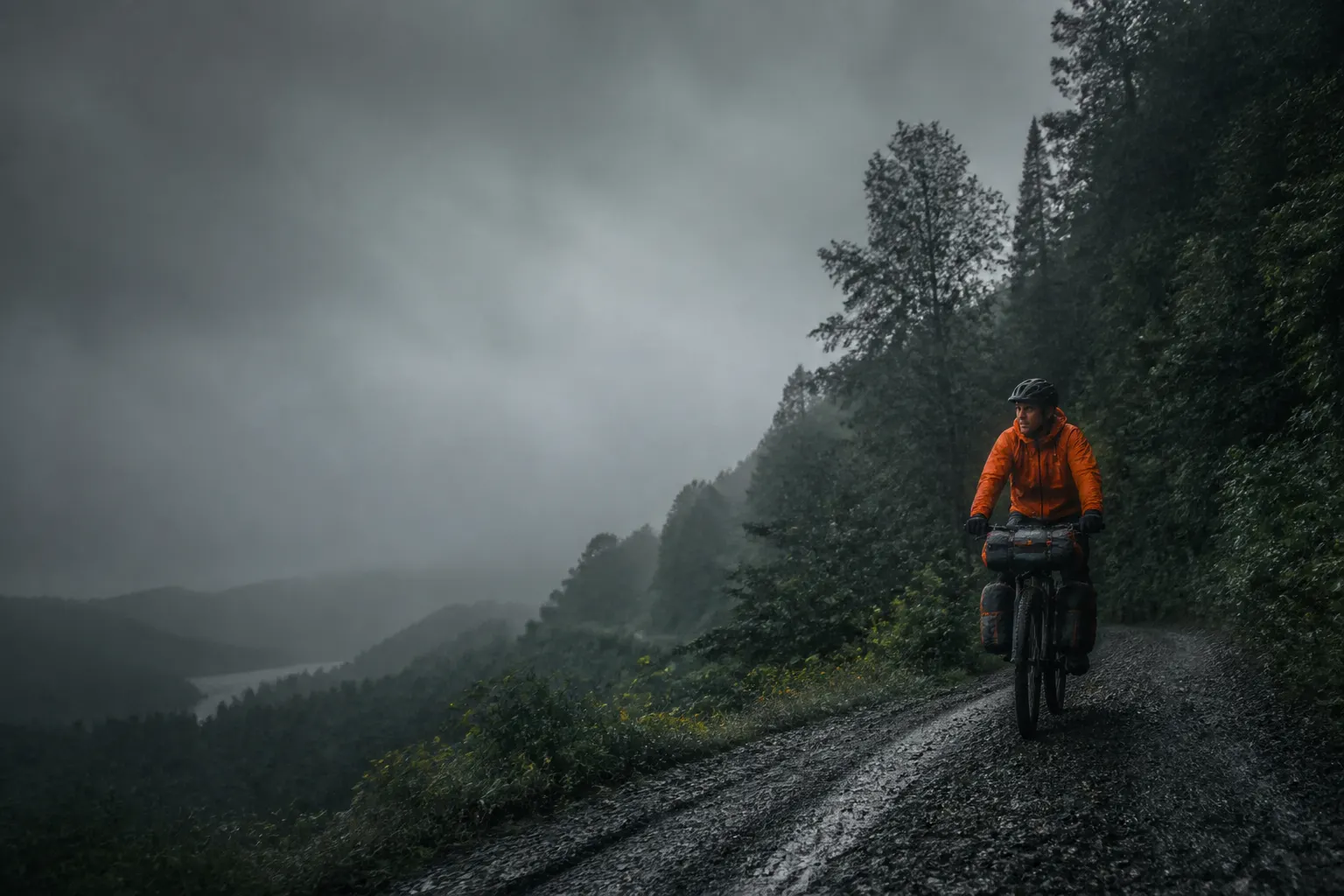 Ciclista recorriendo un camino de ripio mojado entre bosque nativo y niebla sureña.