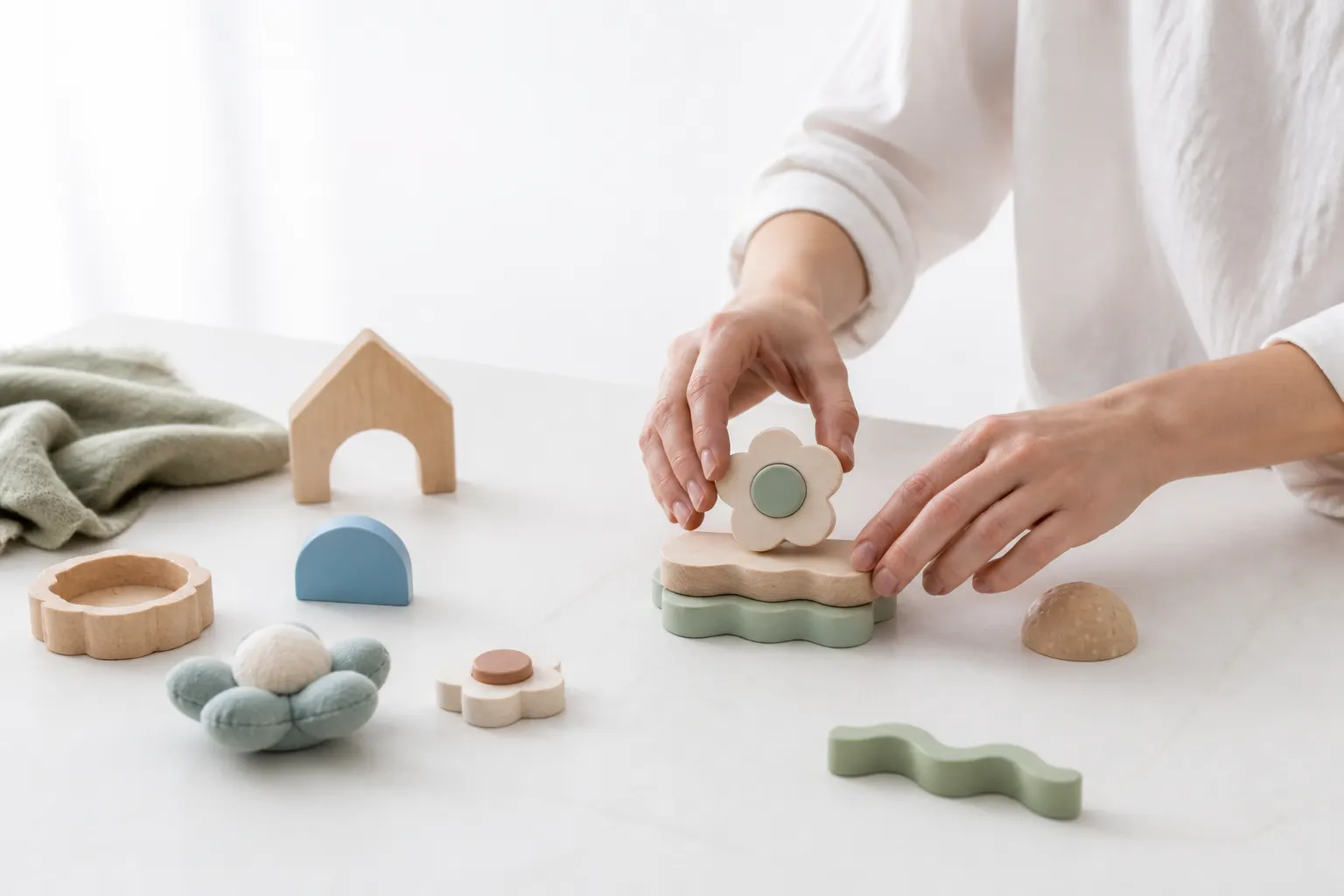Manos organizando pocos objetos sensoriales de madera, tela y silicona en una mesa clara.