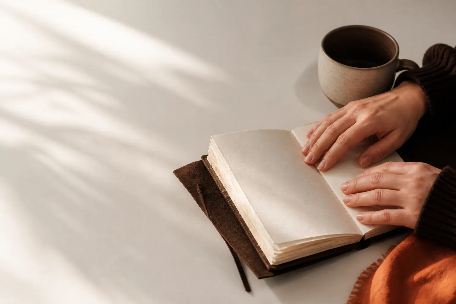 Cuaderno artesanal abierto junto a una taza y manos sobre sus páginas.