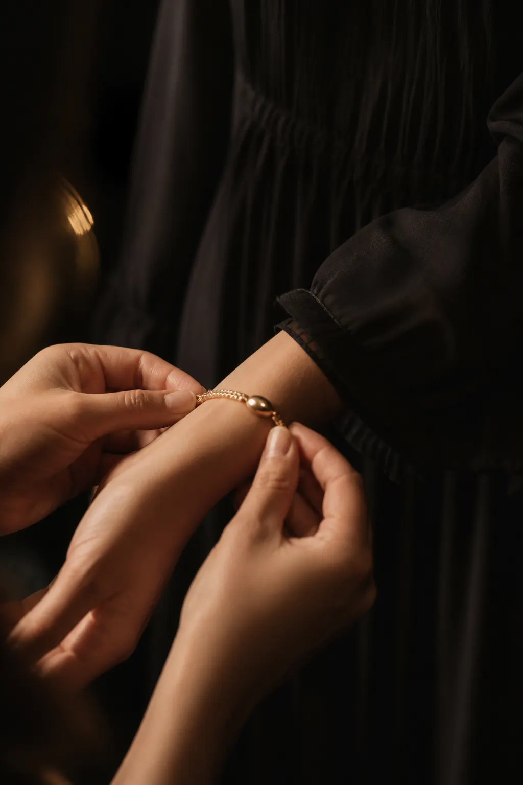 Manos anónimas abrochando una pulsera dorada antes de una ocasión especial, sobre vestido negro.