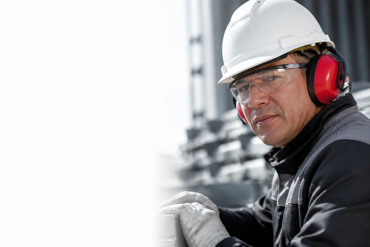 Trabajador equipado con casco, lentes, guantes y protección auditiva en una faena industrial.