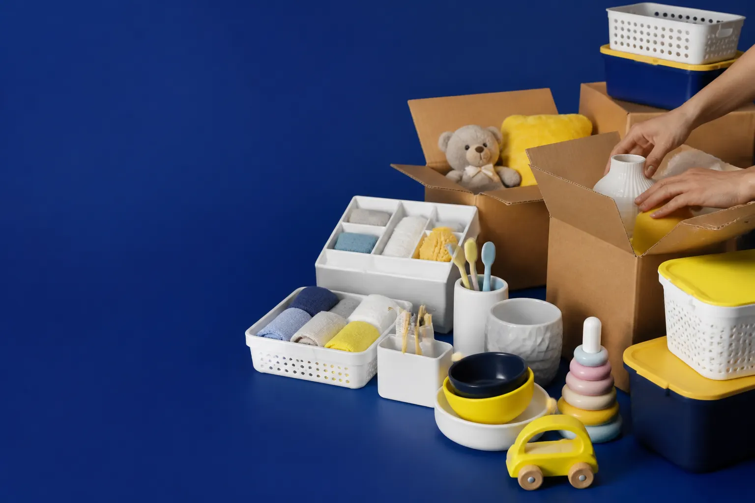 Manos preparando cajas con productos variados para el hogar y la familia sobre un fondo azul profundo