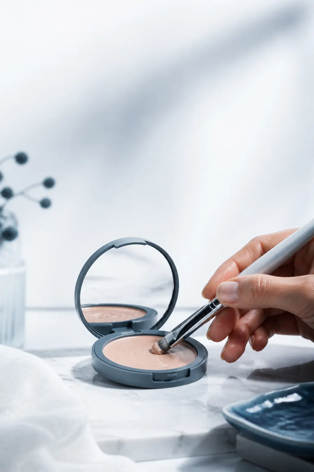 Pincel aplicando maquillaje sobre una paleta neutra sin marcas.