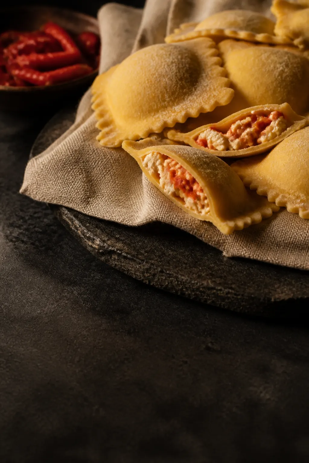 Ravioli artesanales rellenos sobre lino crudo y piedra oscura, con sus pliegues visibles.