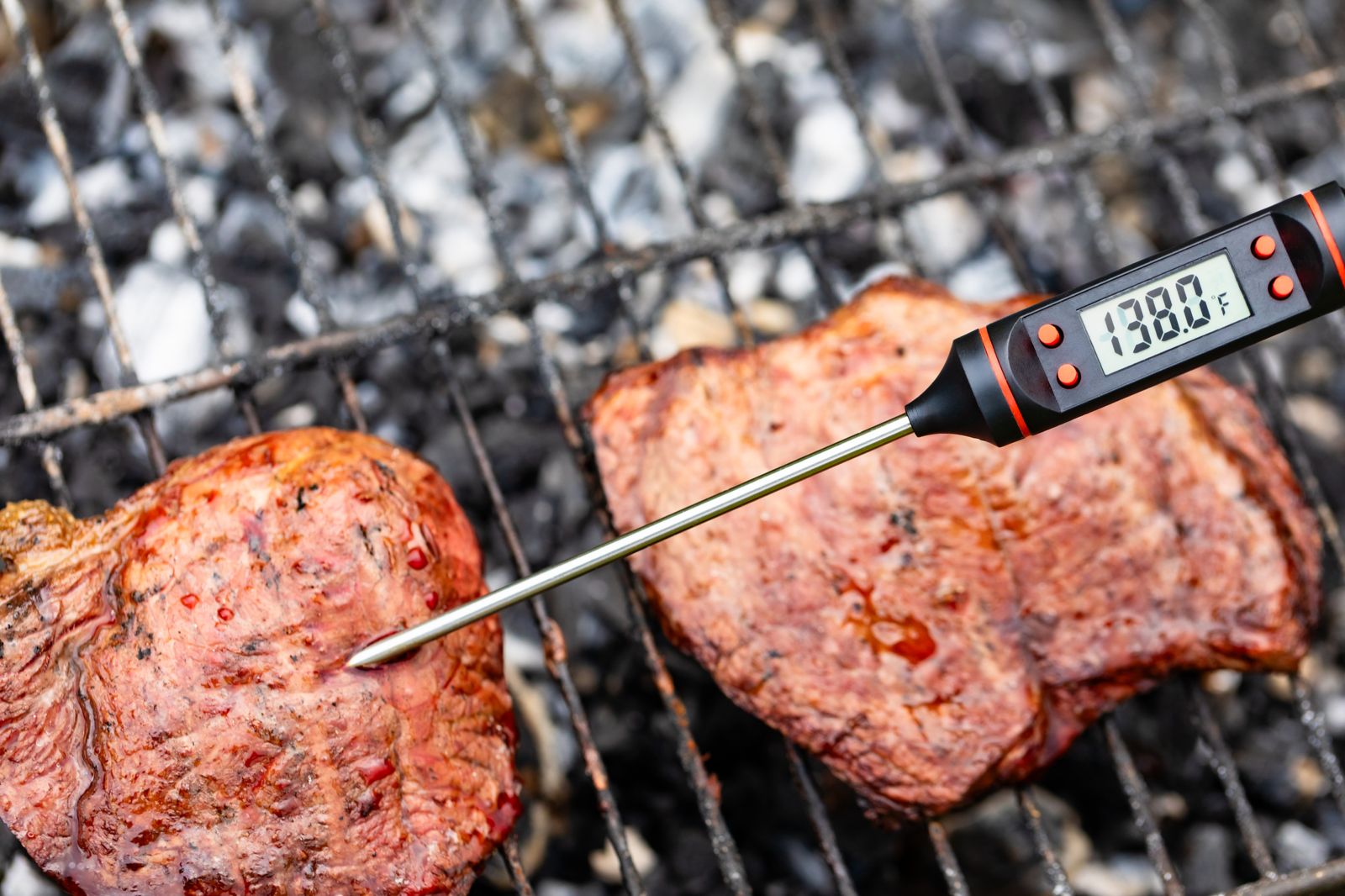 Termómetro digital clavado en un bife sobre la parrilla con brasas