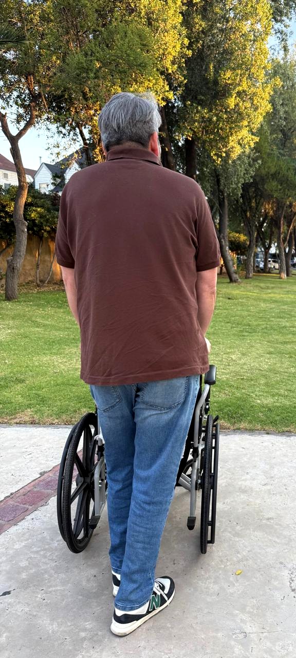 Cuidador acompañando a un adulto mayor en silla de ruedas en un parque