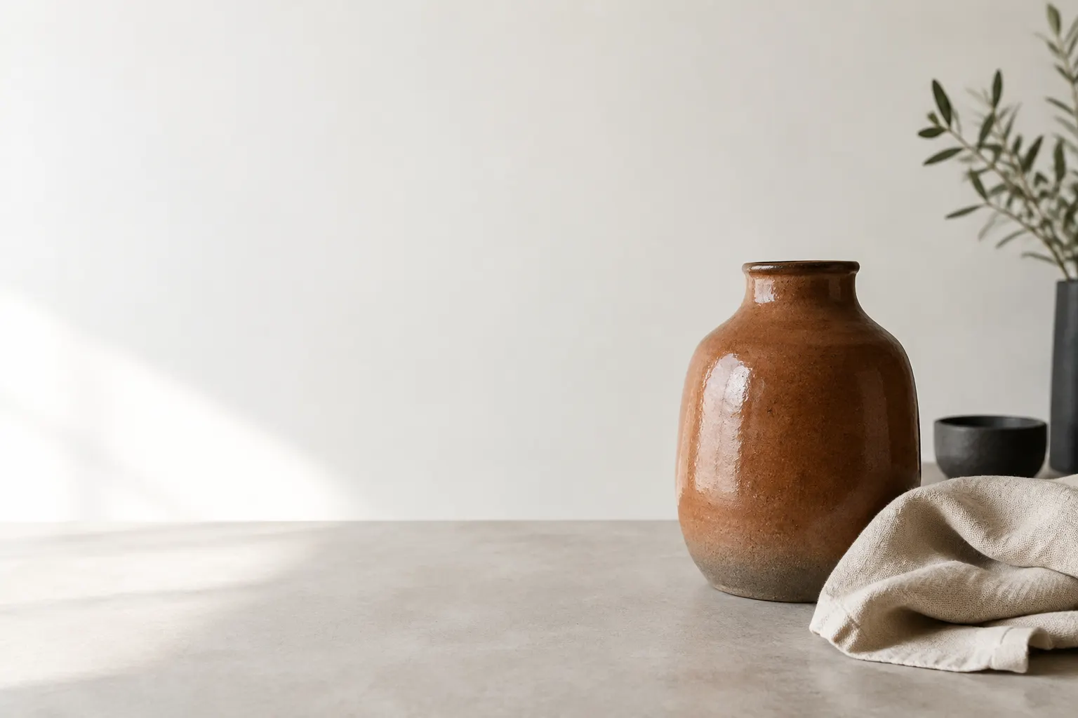 Una pieza de gres terracota junto a un paño de lino sobre una mesa clara.