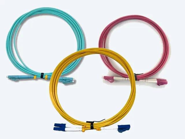 Tres jumpers de fibra óptica enrollados: multimodo OM3 aqua, OM4 magenta y monomodo amarillo con conectores LC.
