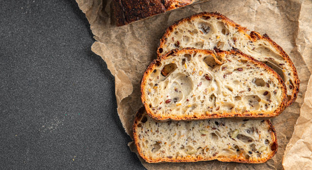 Rebanadas de pan integral de masa madre mostrando miga alveolada, semillas visibles y fermentación lenta bien desarrollada.