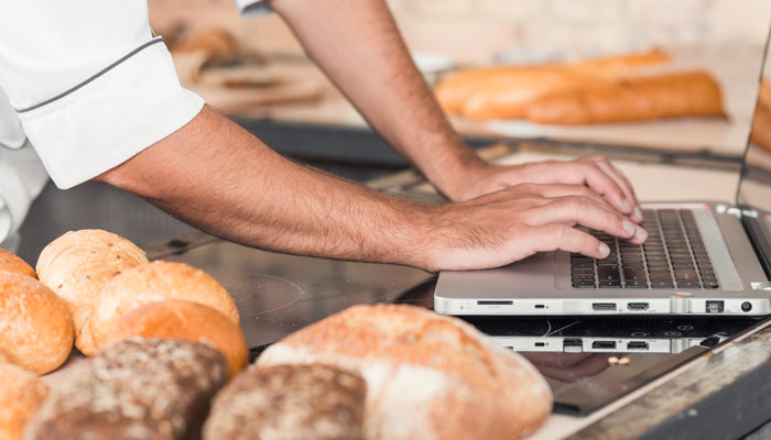 Panadería artesanal combinando oficio y gestión, con panes recién horneados junto a trabajo digital de planificación y pedidos.