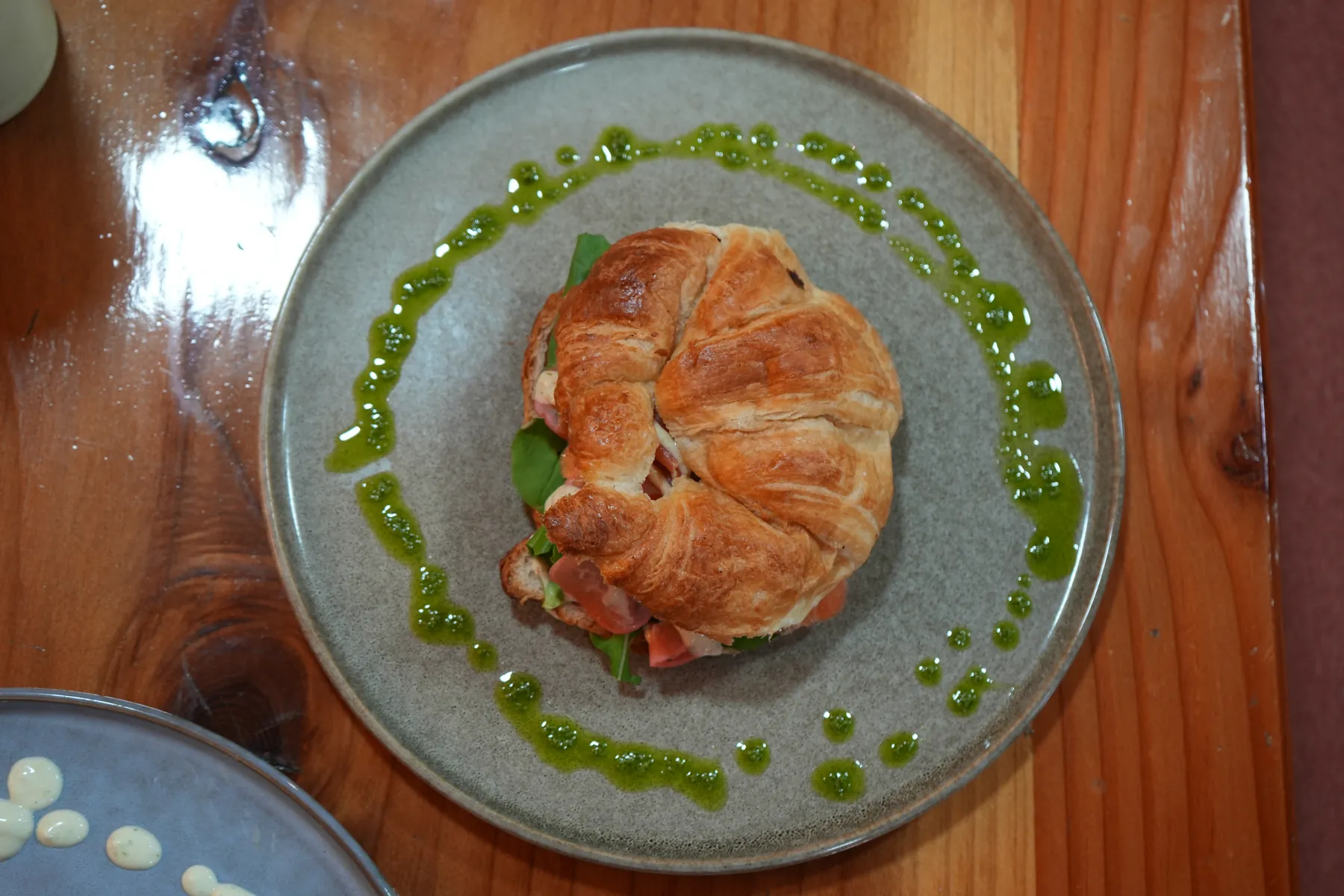 Croissant relleno sobre plato gris con salsa verde