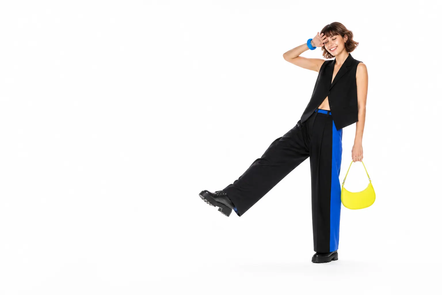 Persona con un look completo negro, azul eléctrico y amarillo ácido, posando de forma espontánea sobre fondo blanco.