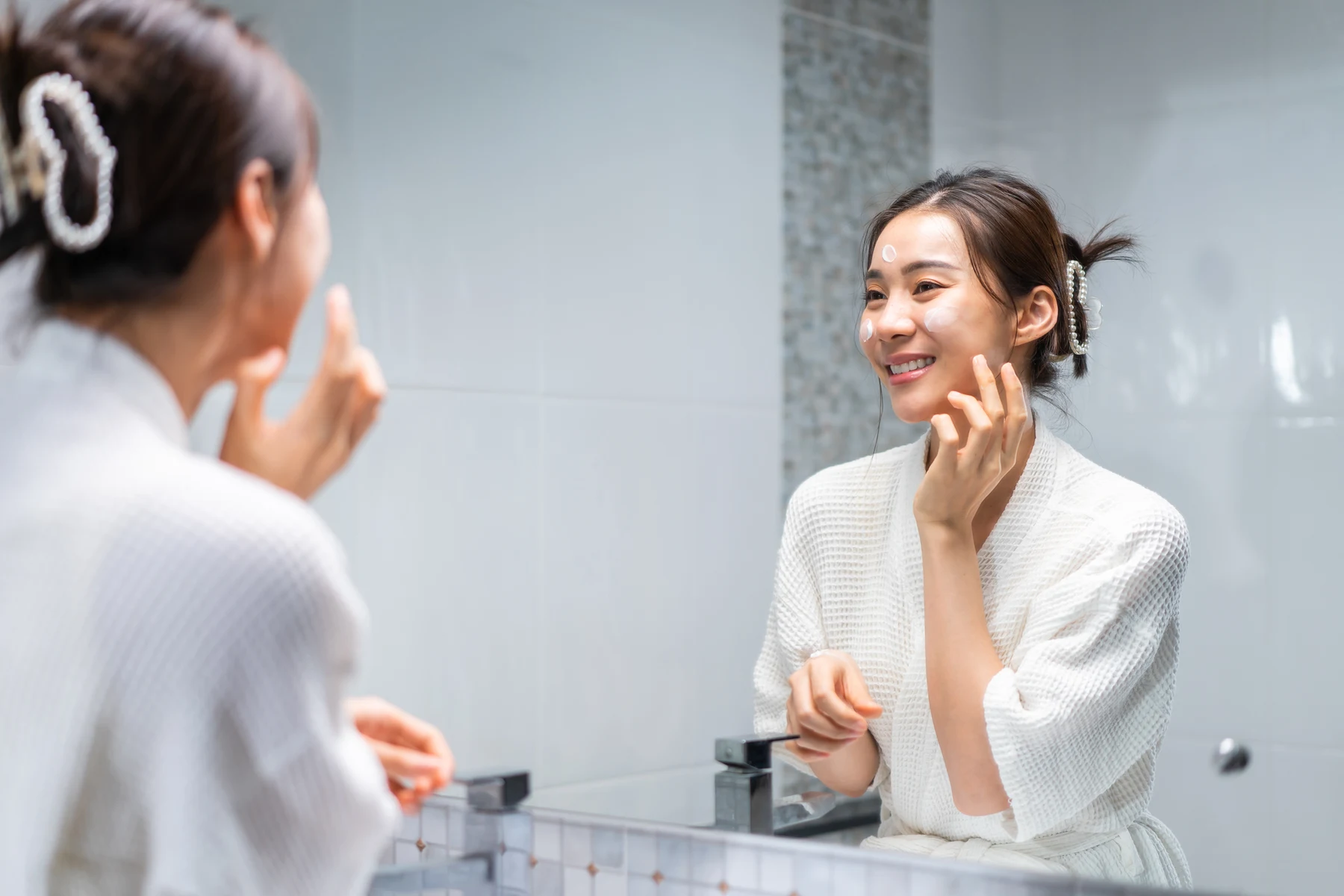 Mujer aplicando crema facial frente al espejo