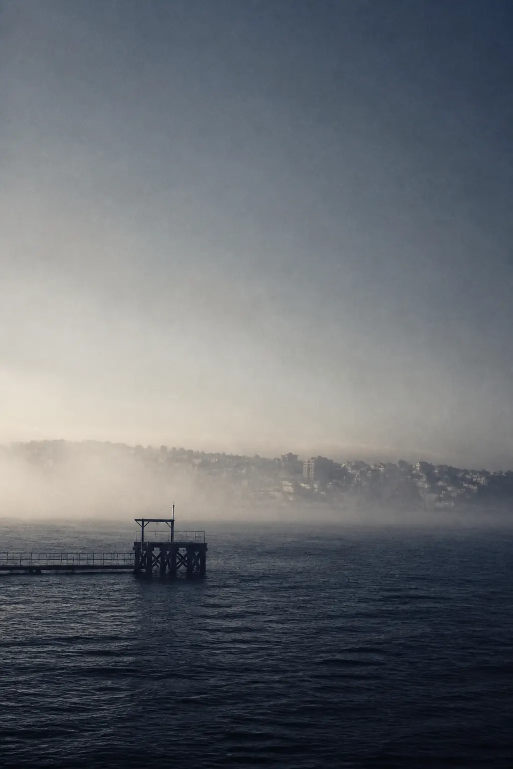 Agua oscura, niebla marina y horizonte apenas visible desde un muelle.