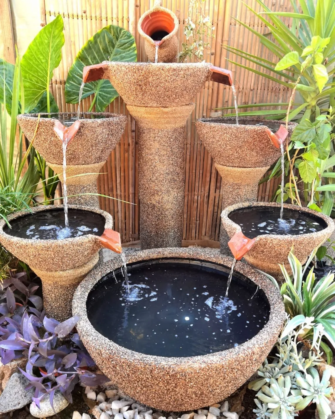 Fuente de agua de varios niveles en tonos naturales entre plantas