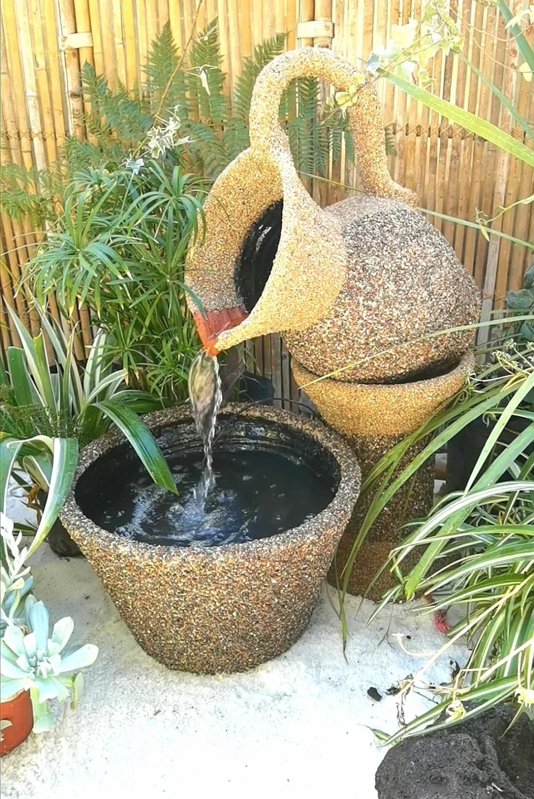Fuente artesanal en forma de jarra entre flores y plantas