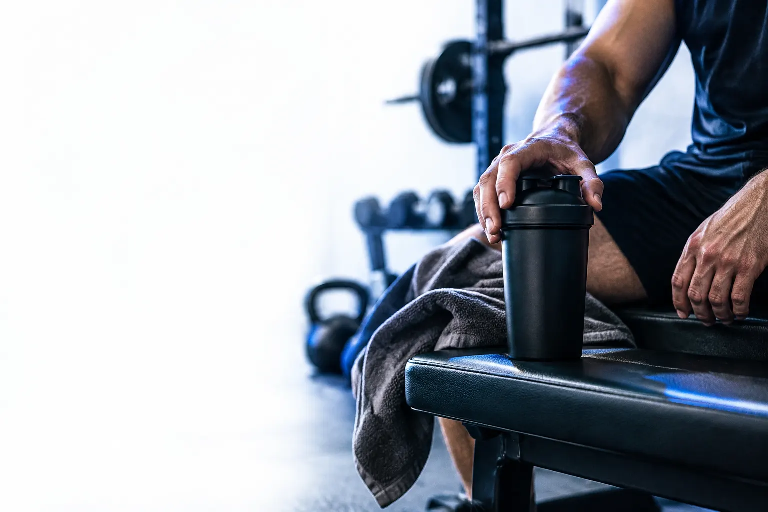 Un shaker negro y una toalla descansan sobre un banco de gimnasio tras el entrenamiento.
