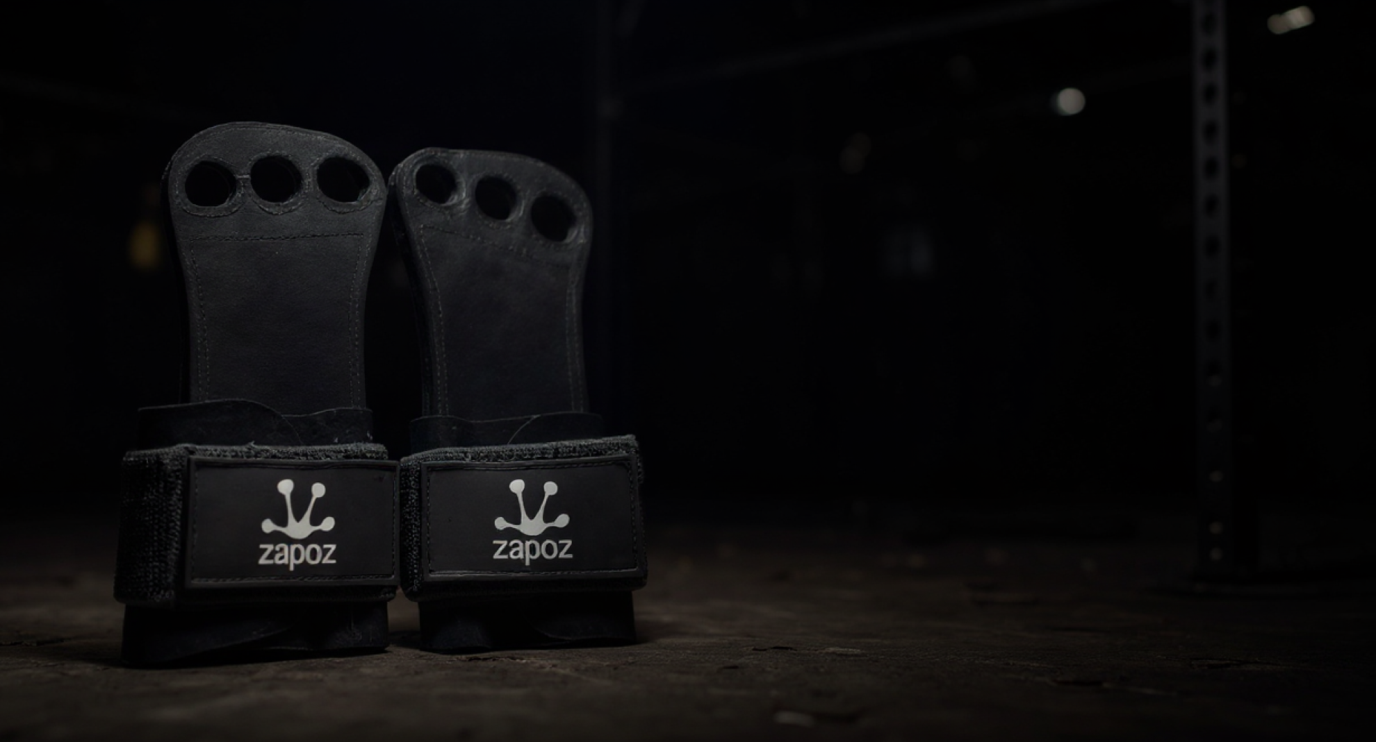 Par de calleras negras Zapoz de cuero genuino sobre piso de box de CrossFit, con fondo oscuro y barra de entrenamiento