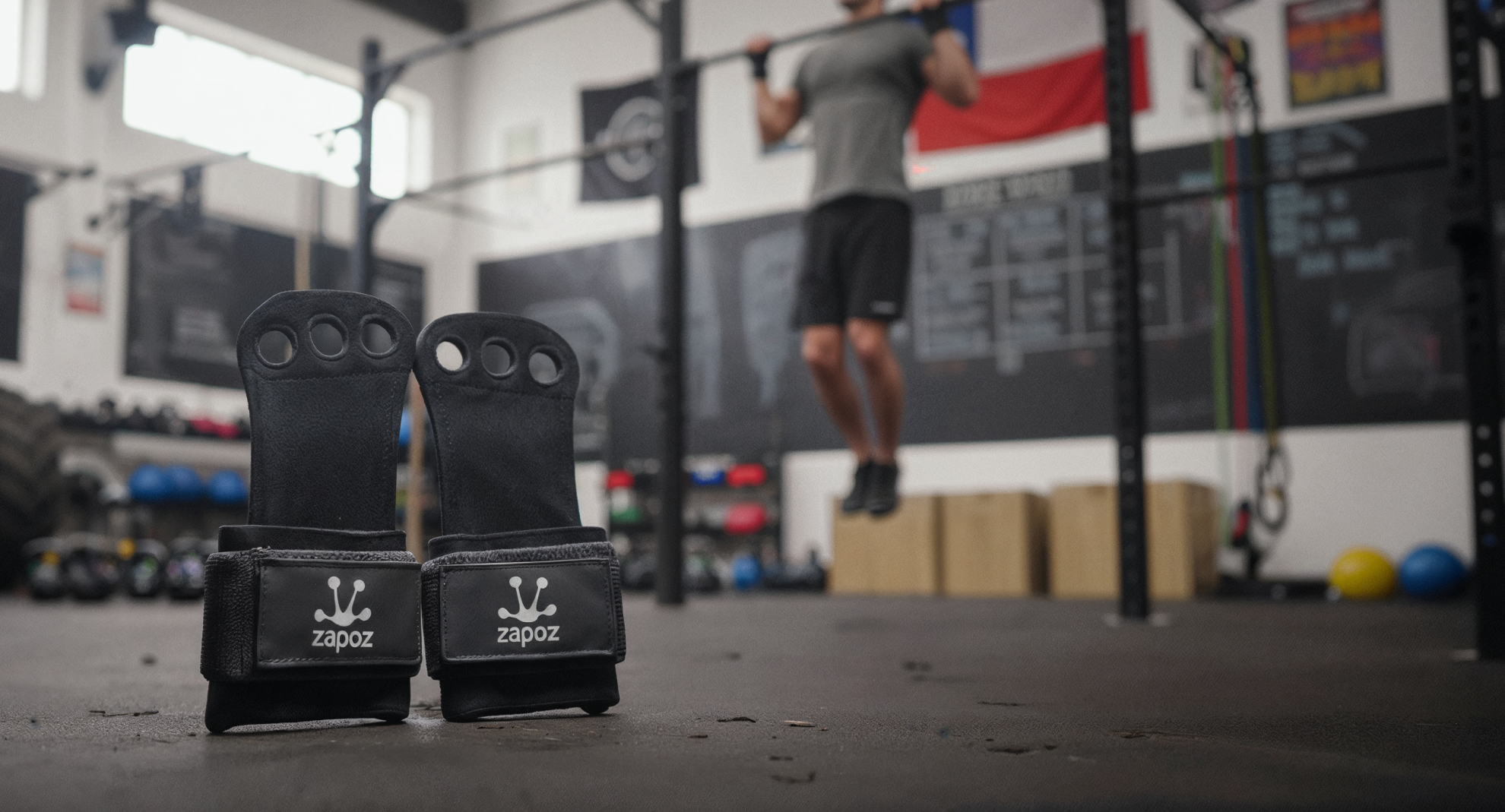 Par de calleras negras Zapoz de cuero genuino sobre piso de box de CrossFit, con fondo oscuro y barra de entrenamiento