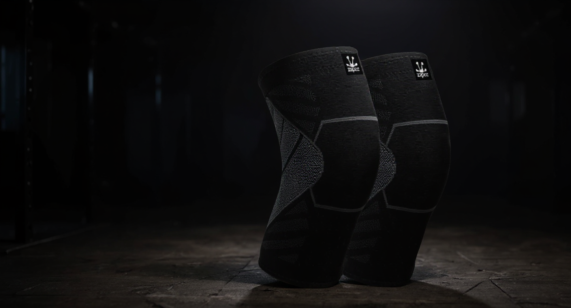 Par de rodilleras de compresión negras Zapoz sobre piso de box de CrossFit, con fondo oscuro e iluminación dramática