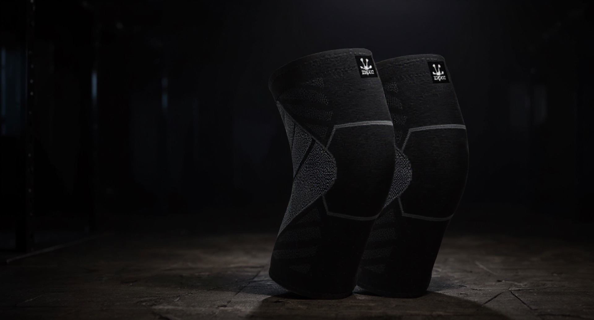 Rodilleras negras Zapoz de compresión ergonómica sobre piso de gimnasio, destacadas con fondo oscuro